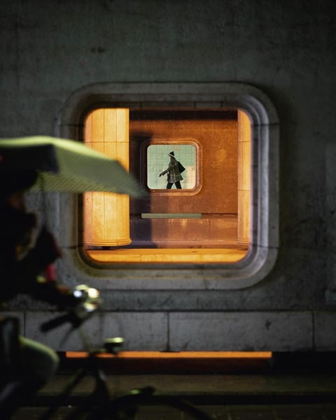 A person seen through a rounded window in a dark concrete wall, lit in warm orange